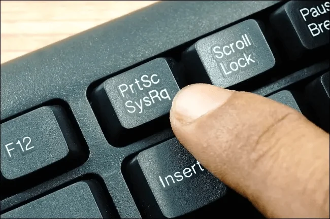 dedo de pessoa branca pressionando a tecla de Print Screen no teclado.