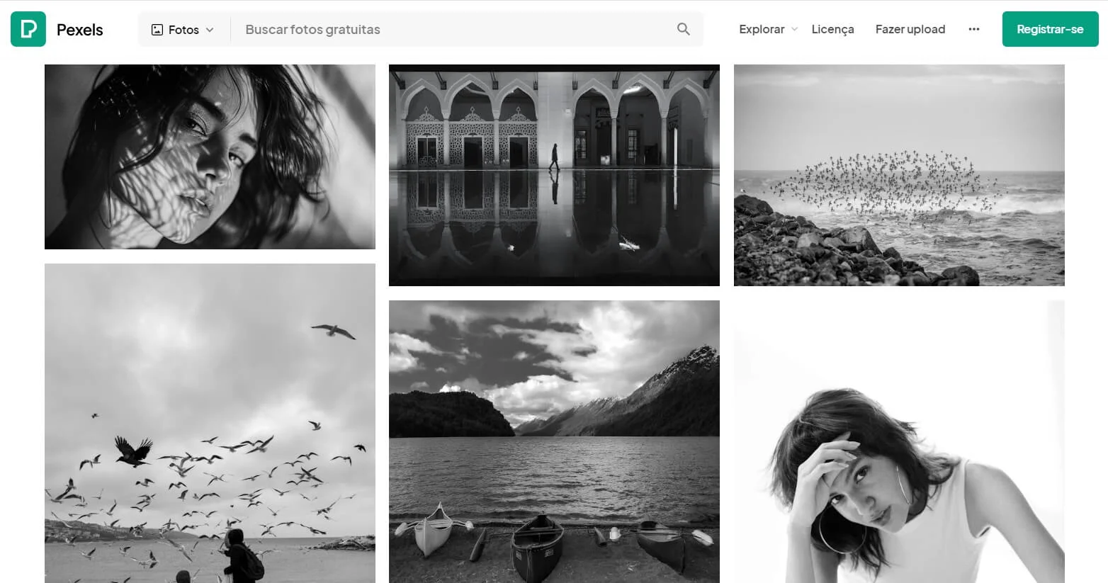 Tela do banco de imagens gratuitas Pexels com uma mulher com seu cabelo ao vento e uma pose com a mão na testa, uma pessoa caminhando, barcos na margem, um grande bando de pássaros, tudo em preto e branco