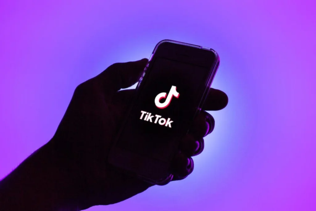 Sombra de uma mão segurando um celular com a tela de abertura do TikTok.