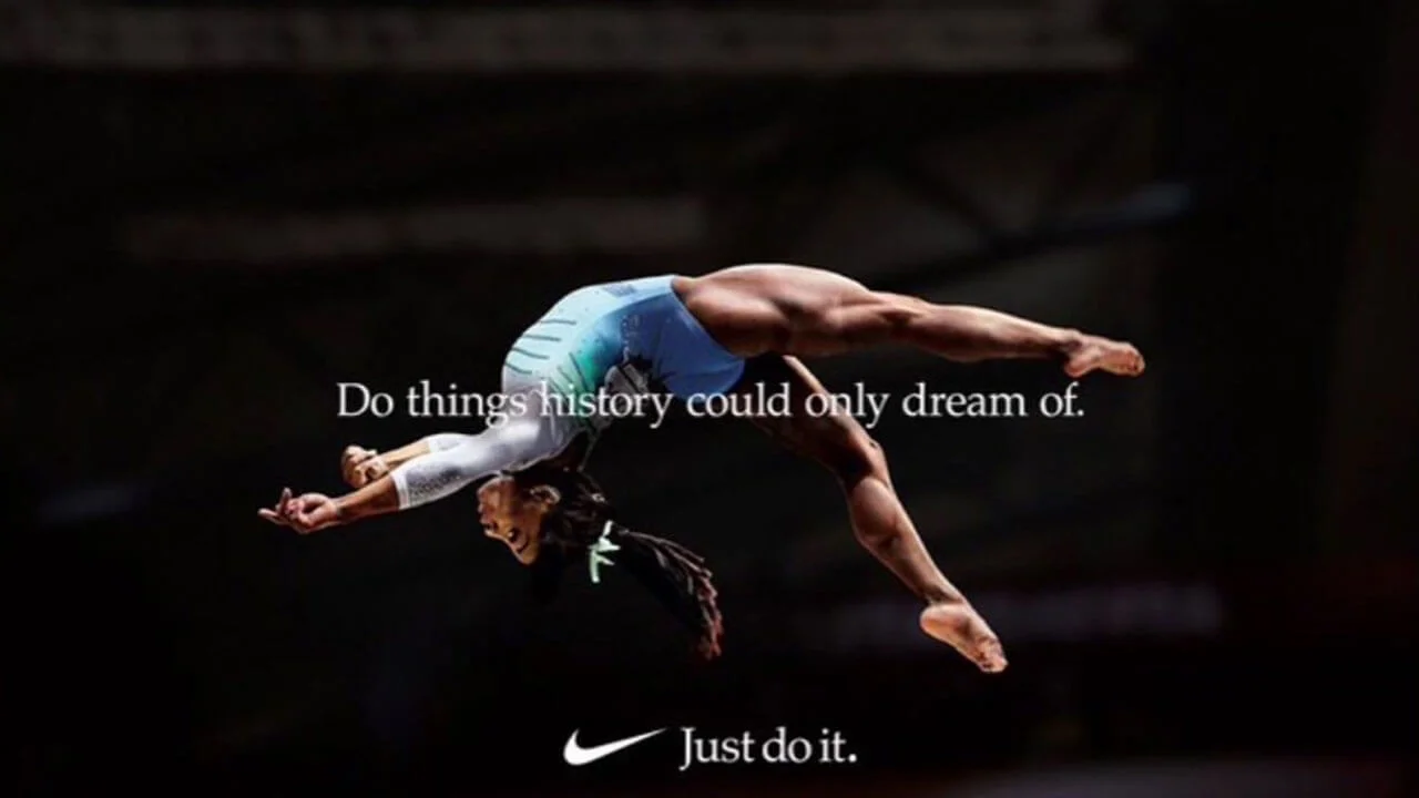 Anúncio da Nike que mostra a ginasta Simone Biles em um salto, com a legenda “do things history could only dream of”, ou seja, “faça coisas com as quais a história poderia apenas sonhar”, seguida pelo slogan da marca: “just do it”, inglês para “apenas faça”.