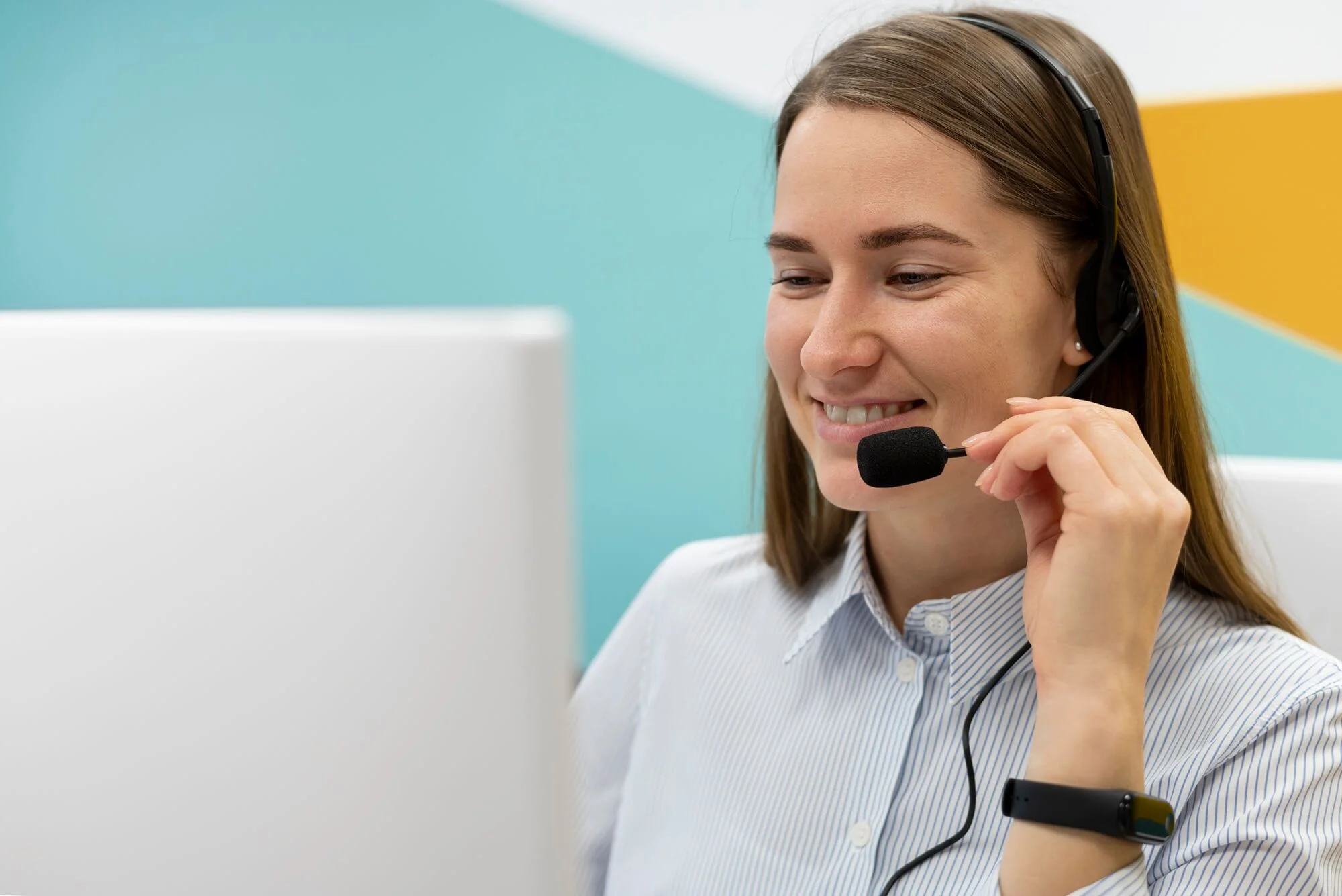 Foto de uma mulher com um headset, olhando para a tela de um computador e sorrindo.