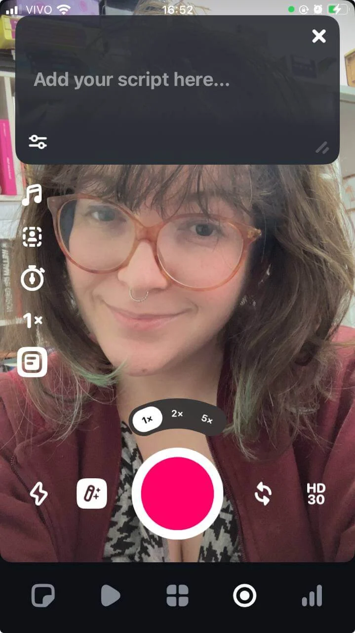 Imagem de uma câmera frontal aberta no app Edits, mostrando uma pessoa branca com cabelos castanhos e de franja. No topo da tela há um box com o texto “Add your script here” (Coloque seu roteiro aqui). O ícone que abre o teleprompter é o último de uma fileira à esquerda da tela.