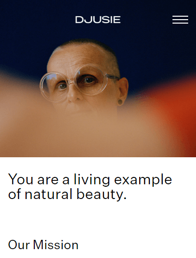 The top of the “Our Mission” page features a photo of an older woman with a buzz cut and big round glasses. The text under the photo reads: “You are a living example of natural beauty”