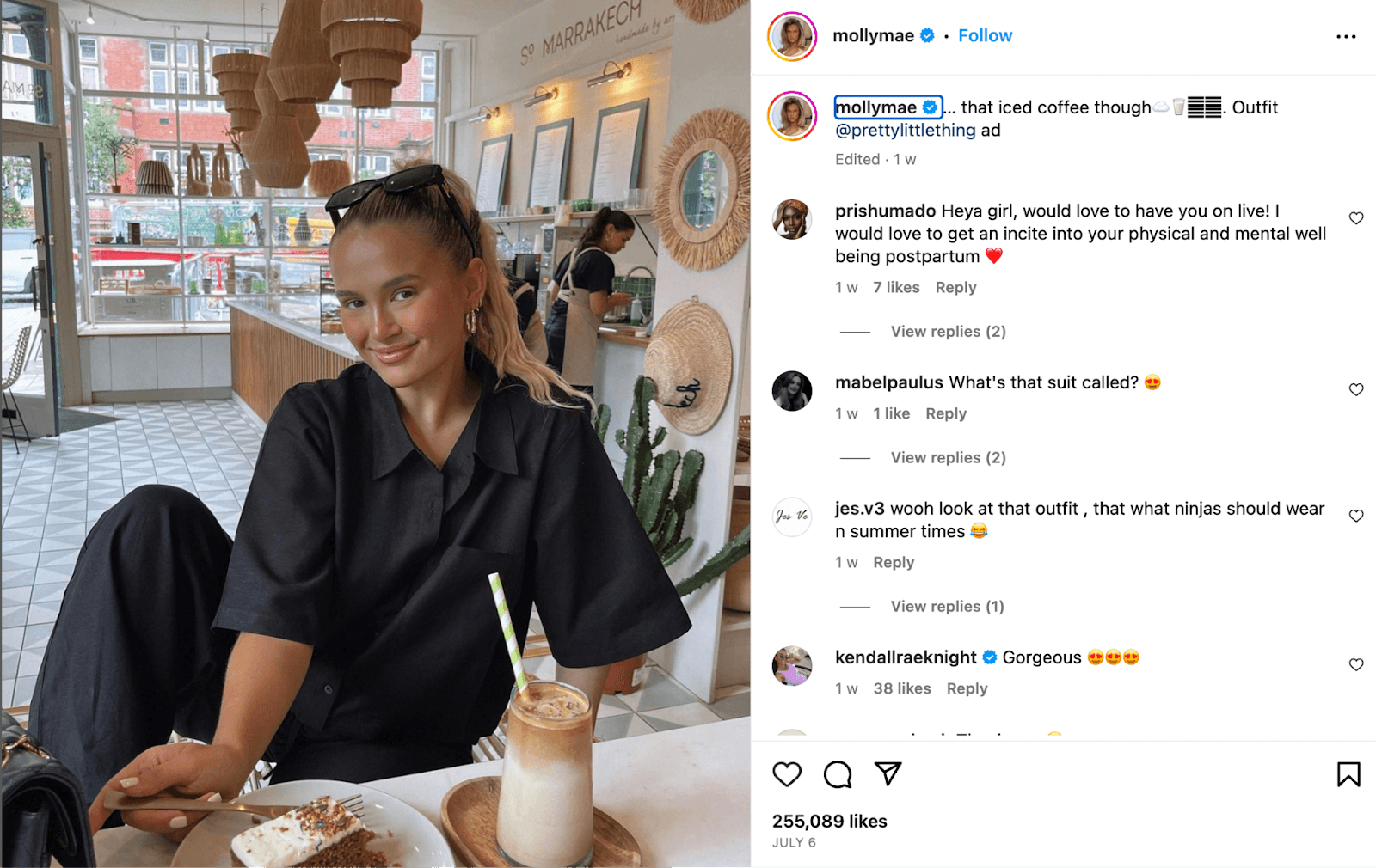 Instagram influencer post of a woman sat in a coffee shop drinking an iced coffee, wearing a black jumpsuit and promoting where she bought her outfit from.